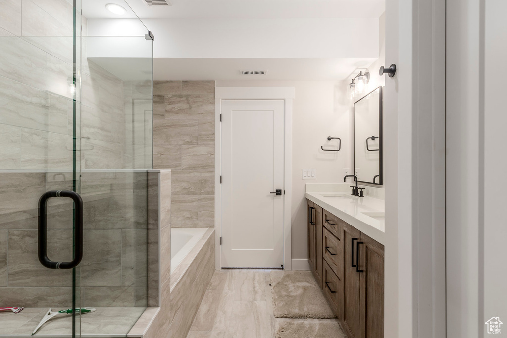 Full bath featuring a stall shower, double vanity, tiled tub, and baseboards
