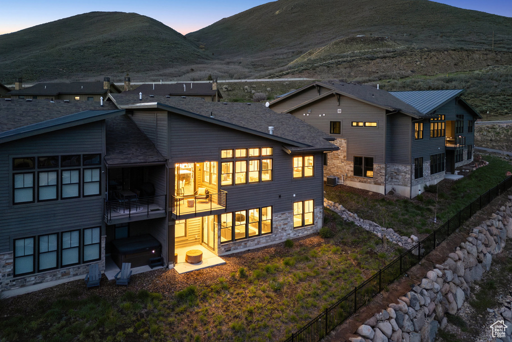 Rear view of house featuring a balcony, a mountain view, fence, and stone siding