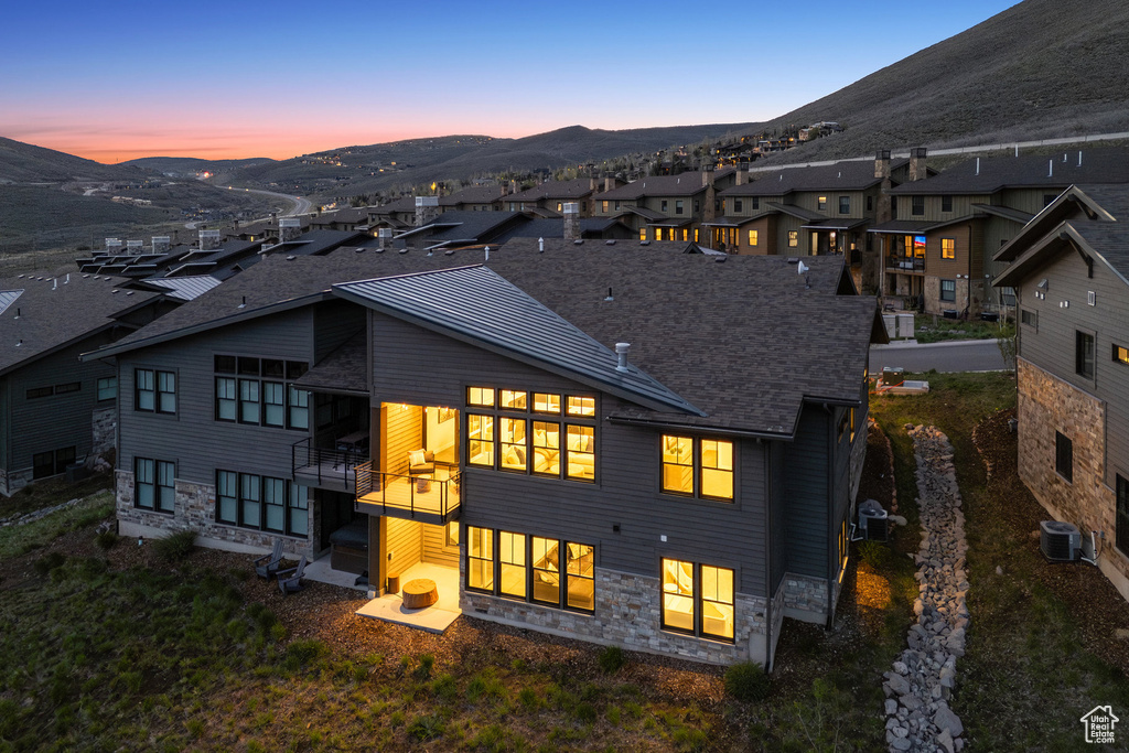 Back of property at dusk with a mountain view, cooling unit, stone siding, and a residential view
