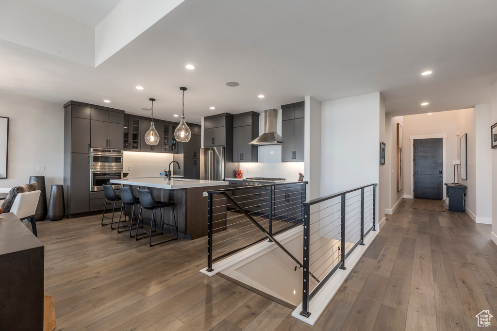 Kitchen with wall chimney exhaust hood, stainless steel appliances, recessed lighting, a breakfast bar, and light wood-style floors