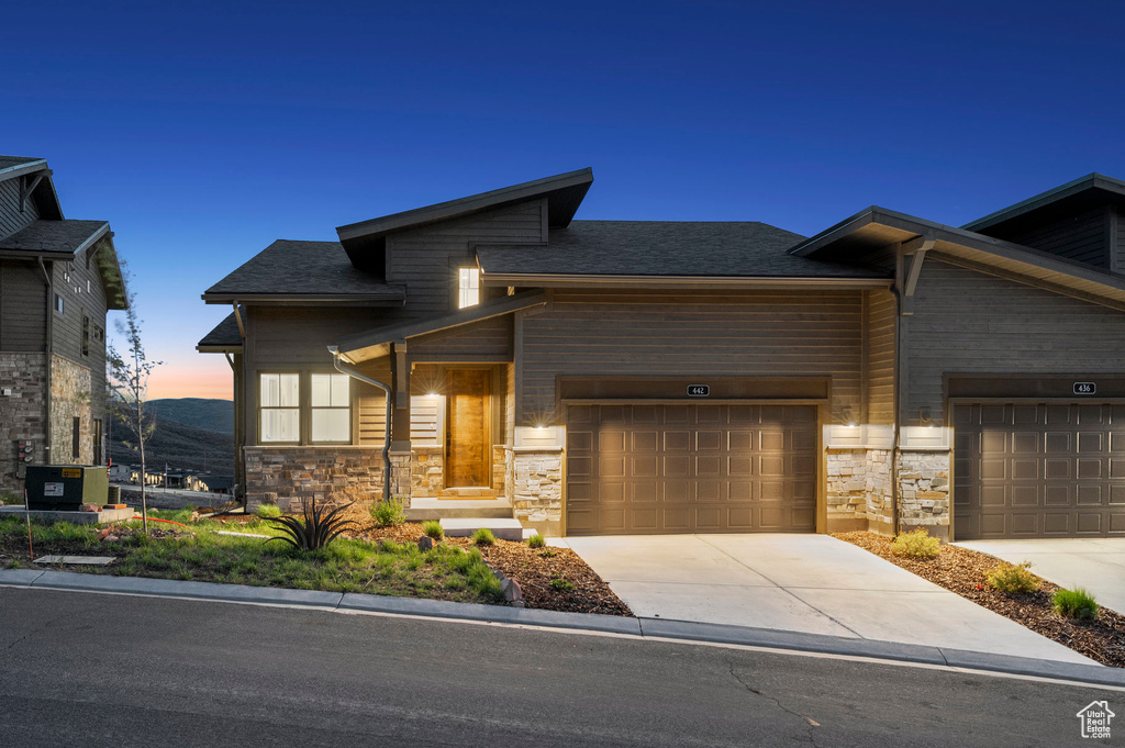 View of front facade featuring stone siding, concrete driveway, a garage, and a shingled roof