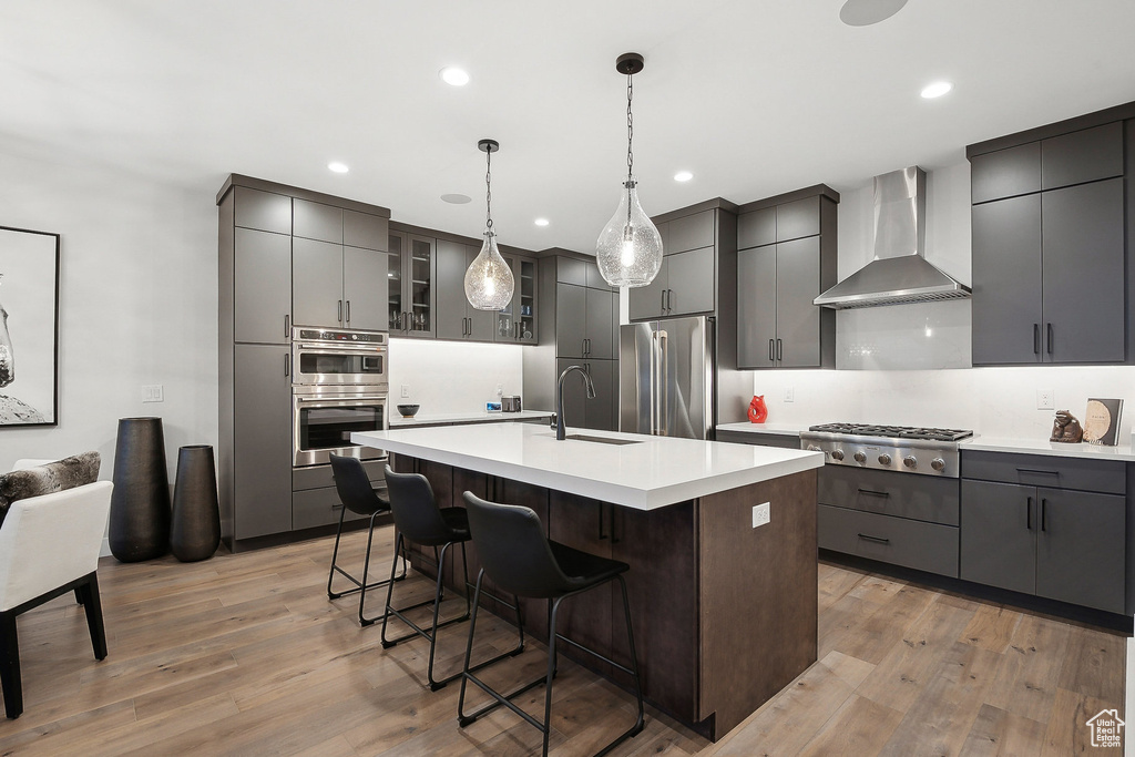 Kitchen with stainless steel appliances, wall chimney range hood, a sink, light wood-type flooring, and recessed lighting