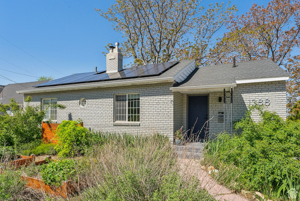 Back of house with brick siding, solar panels, and a chimney