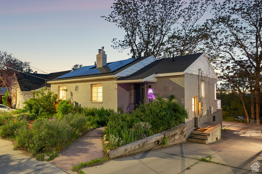 View of front of property featuring a chimney, brick siding, and roof mounted solar panels