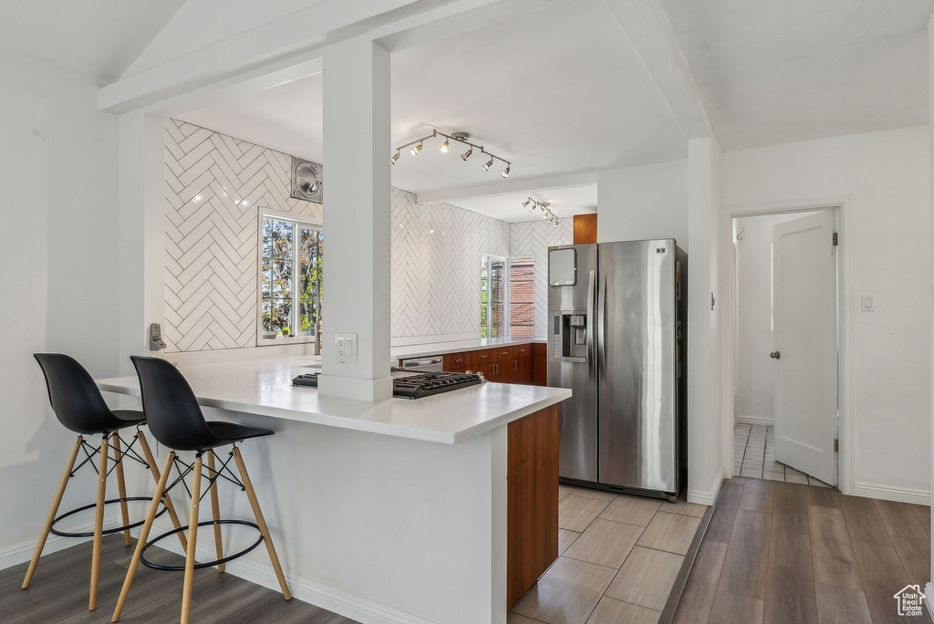 Kitchen featuring a peninsula, light wood-type flooring, a kitchen bar, and stainless steel refrigerator with ice dispenser