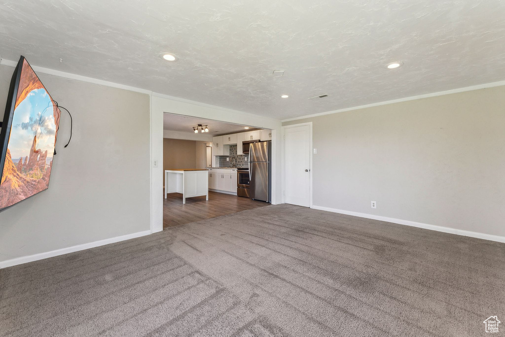 Unfurnished living room with recessed lighting, baseboards, ornamental molding, and dark carpet
