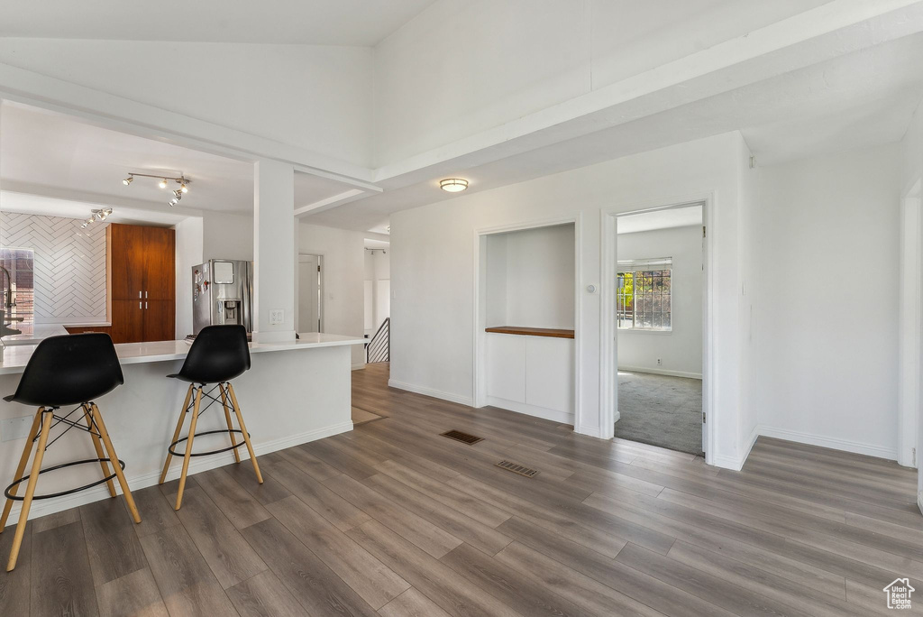 Kitchen with dark wood-style flooring, stainless steel refrigerator with ice dispenser, visible vents, light countertops, and a breakfast bar