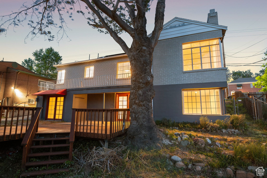 Back of house with fence, a chimney, a wooden deck, and a balcony