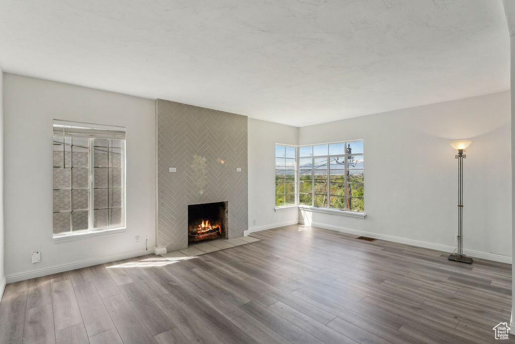 Unfurnished living room featuring baseboards, visible vents, a large fireplace, and wood finished floors