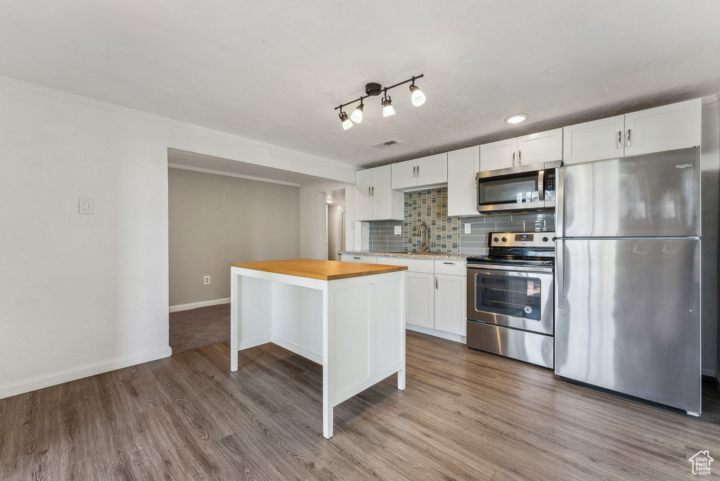 Kitchen featuring tasteful backsplash, wood finished floors, baseboards, stainless steel appliances, and white cabinetry