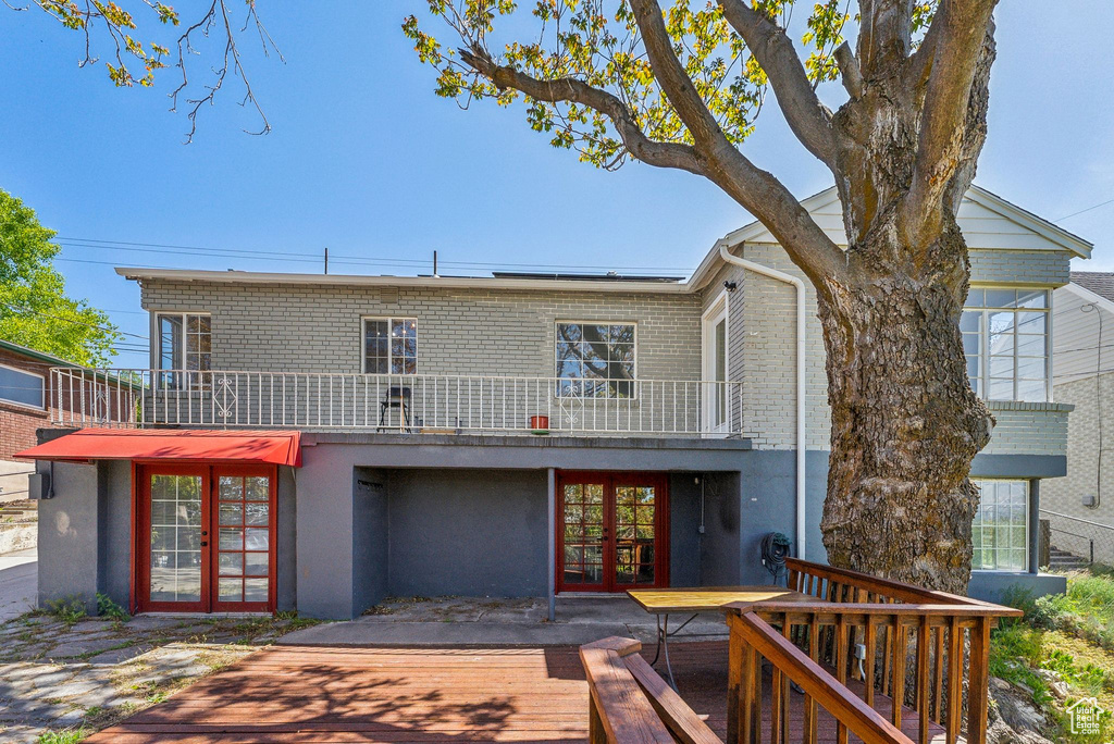 Back of house with brick siding, a deck, french doors, and stucco siding