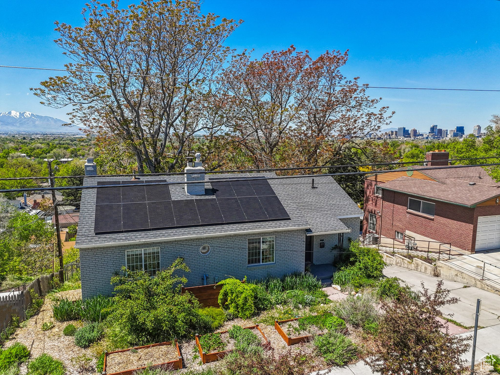 Back of property featuring roof with shingles, a chimney, solar panels, and brick siding
