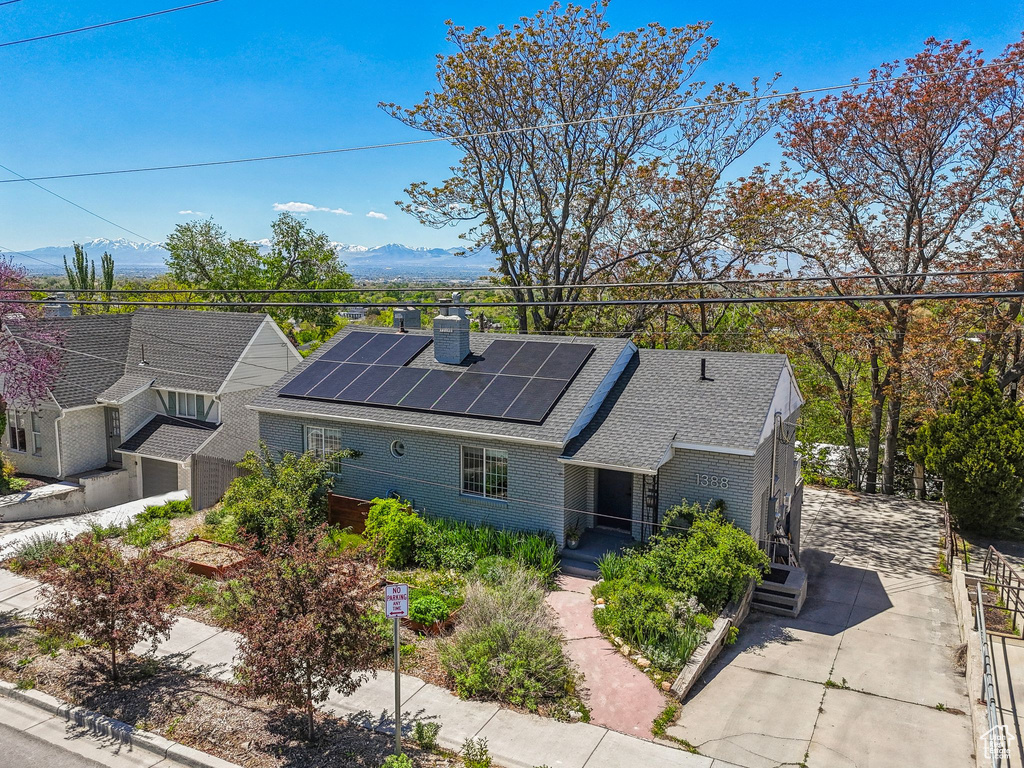 View of front facade featuring a chimney, brick siding, a shingled roof, roof mounted solar panels, and a mountain view