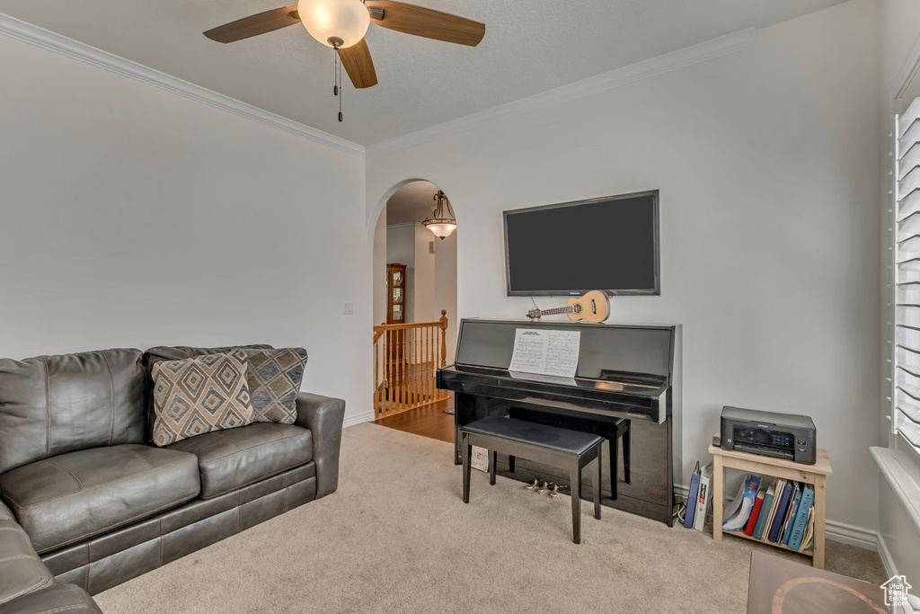 Living area featuring crown molding, ceiling fan, arched walkways, carpet floors, and baseboards