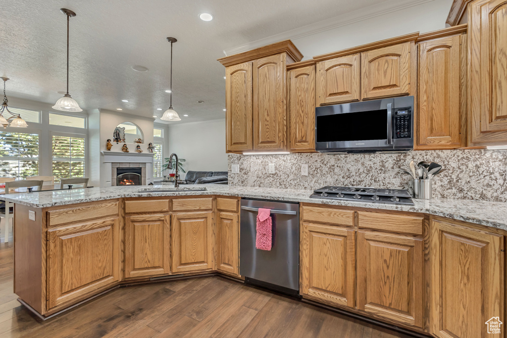 Kitchen featuring appliances with stainless steel finishes, a sink, a peninsula, dark wood-style flooring, and tasteful backsplash