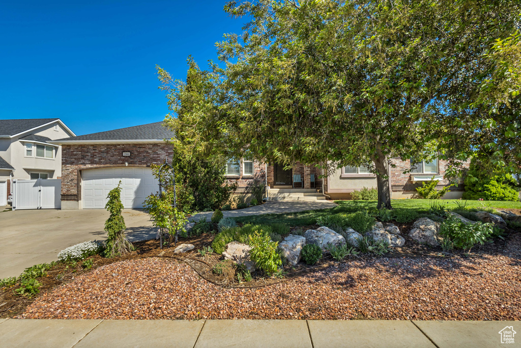 Obstructed view of property featuring concrete driveway, a garage, brick siding, and fence