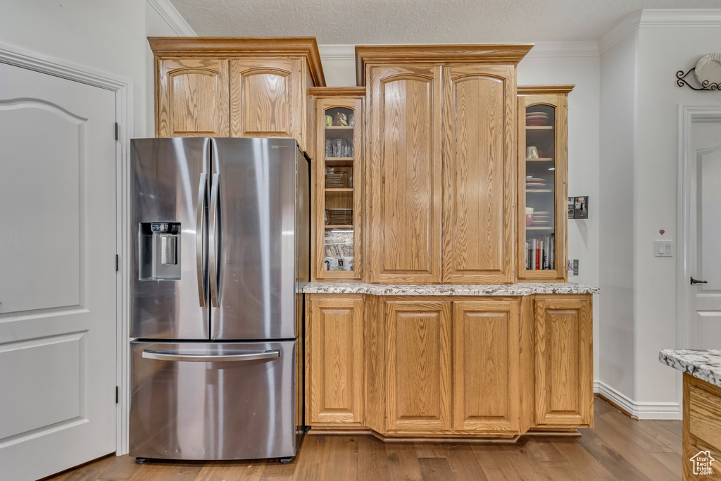 Kitchen featuring stainless steel refrigerator with ice dispenser, ornamental molding, light stone countertops, dark wood-type flooring, and glass insert cabinets