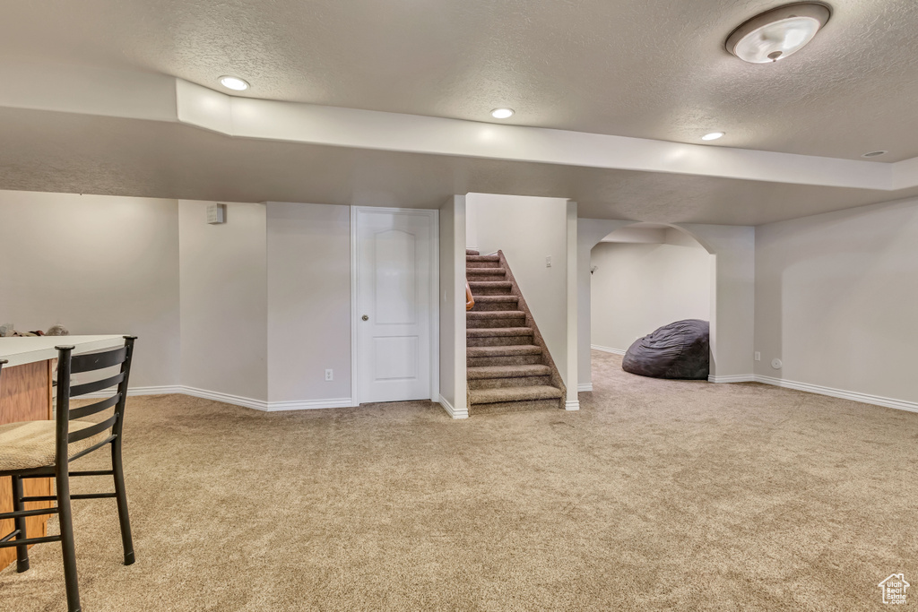 Finished basement featuring a textured ceiling, carpet flooring, baseboards, stairs, and arched walkways