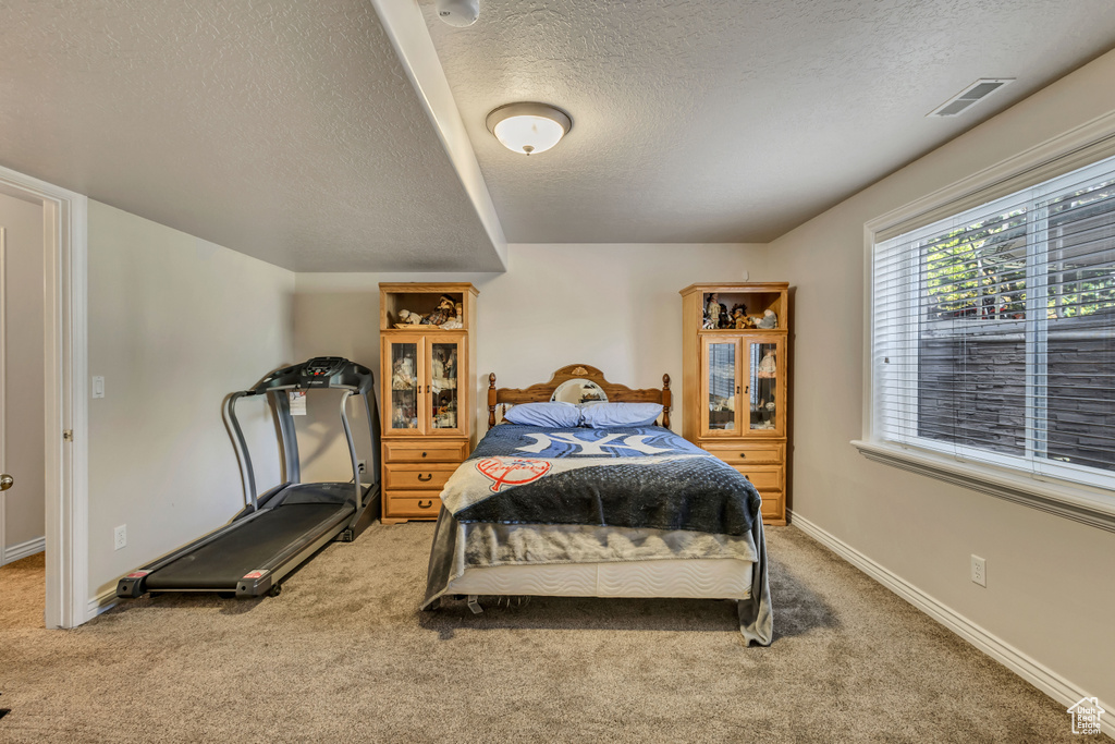 Bedroom with a textured ceiling, light carpet, and baseboards