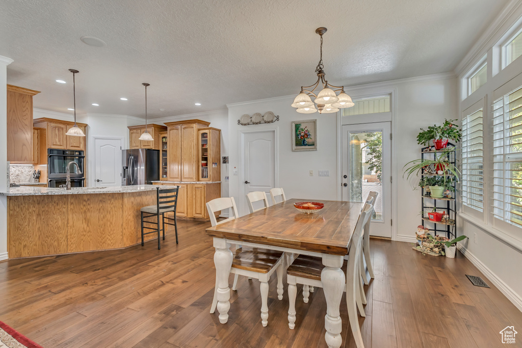 Dining space with plenty of natural light, wood finished floors, crown molding, recessed lighting, and a chandelier