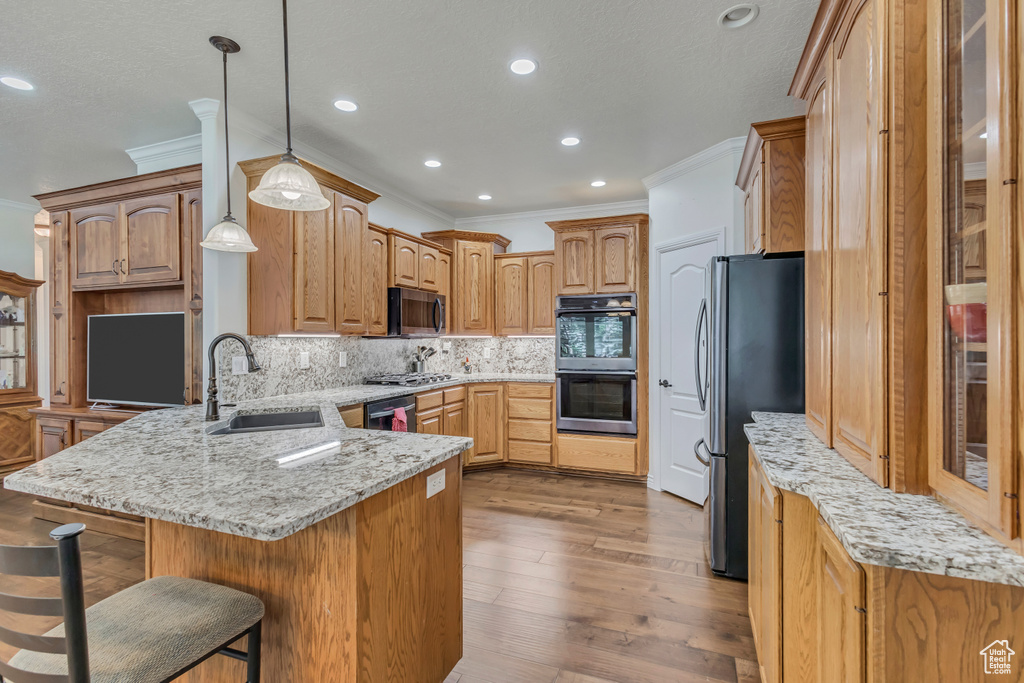 Kitchen featuring stainless steel appliances, a sink, ornamental molding, a peninsula, and tasteful backsplash