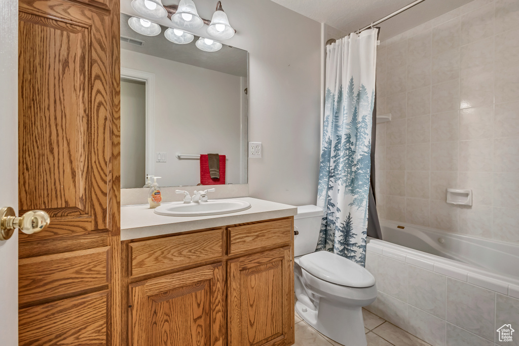 Full bathroom with tile patterned floors, toilet, vanity, and tiled shower / bath combo