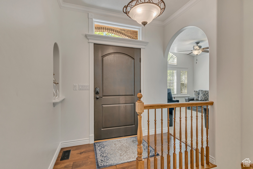 Entrance foyer with arched walkways, crown molding, wood finished floors, a ceiling fan, and baseboards