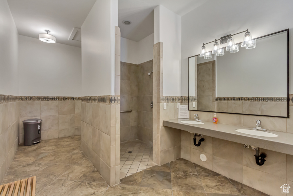 Bathroom featuring a sink, tile walls, walk in shower, and a wainscoted wall