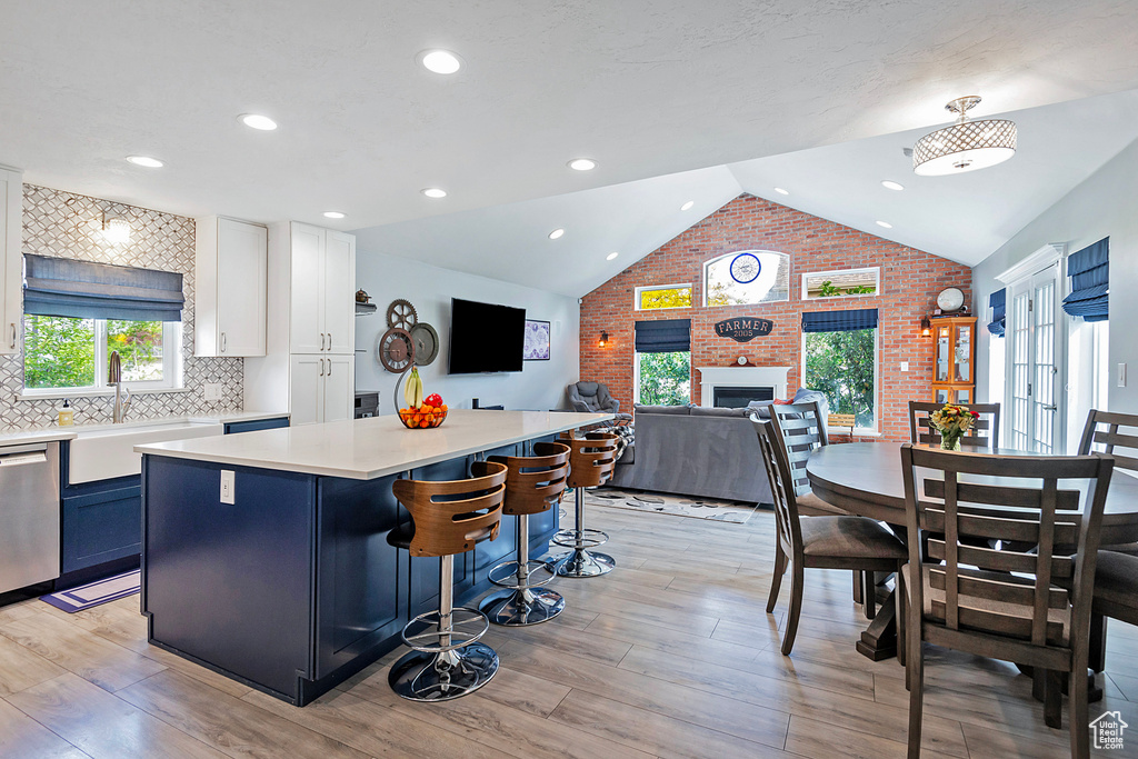 Kitchen featuring a sink, dishwasher, vaulted ceiling, a large fireplace, and a center island