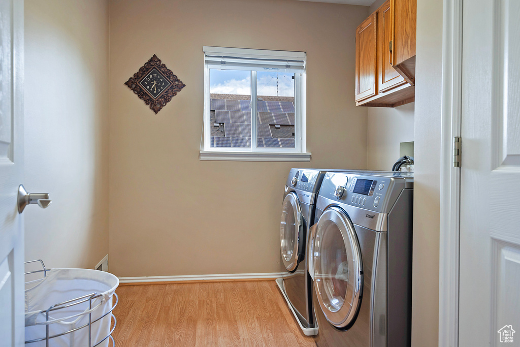 Washroom featuring baseboards, washing machine and dryer, light wood-type flooring, and cabinet space