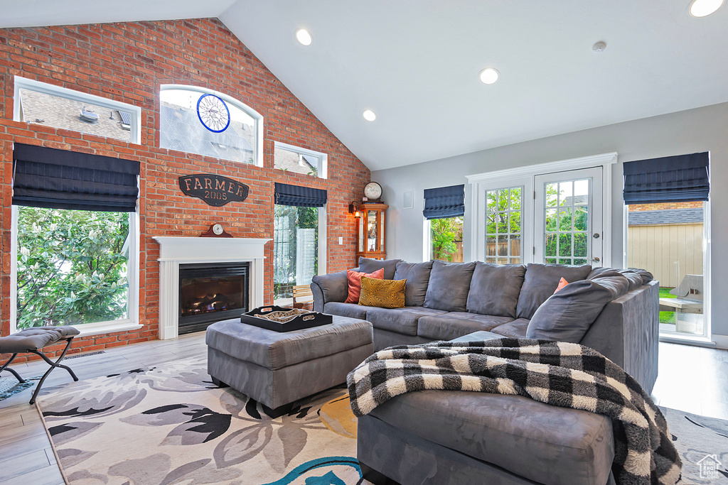 Living room featuring brick wall, high vaulted ceiling, a glass covered fireplace, and wood finished floors