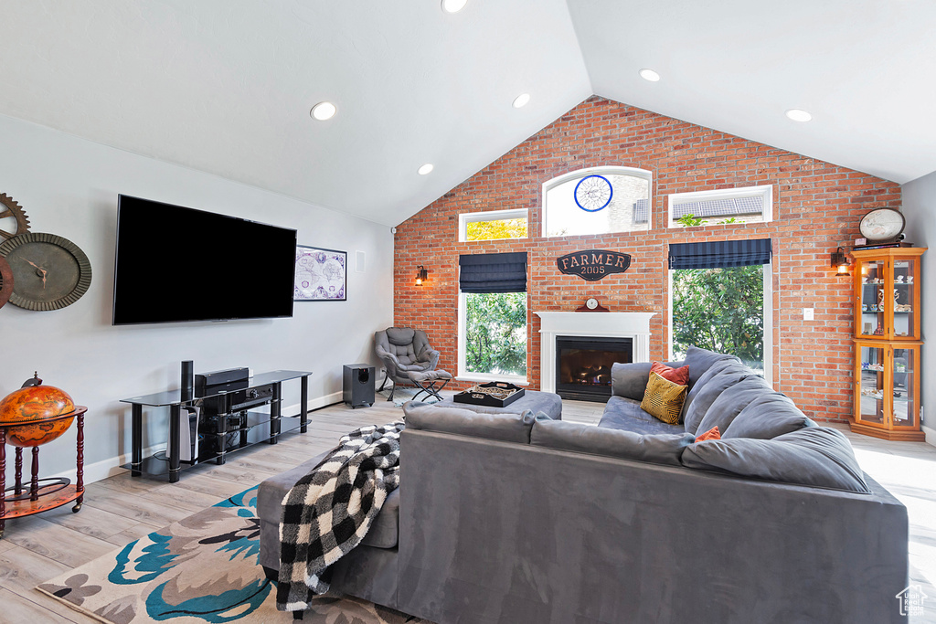 Living room with light wood-style floors, a fireplace, brick wall, and plenty of natural light