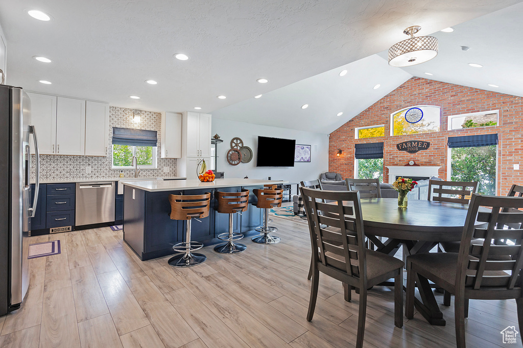 Dining room featuring recessed lighting, brick wall, high vaulted ceiling, and light wood-style flooring