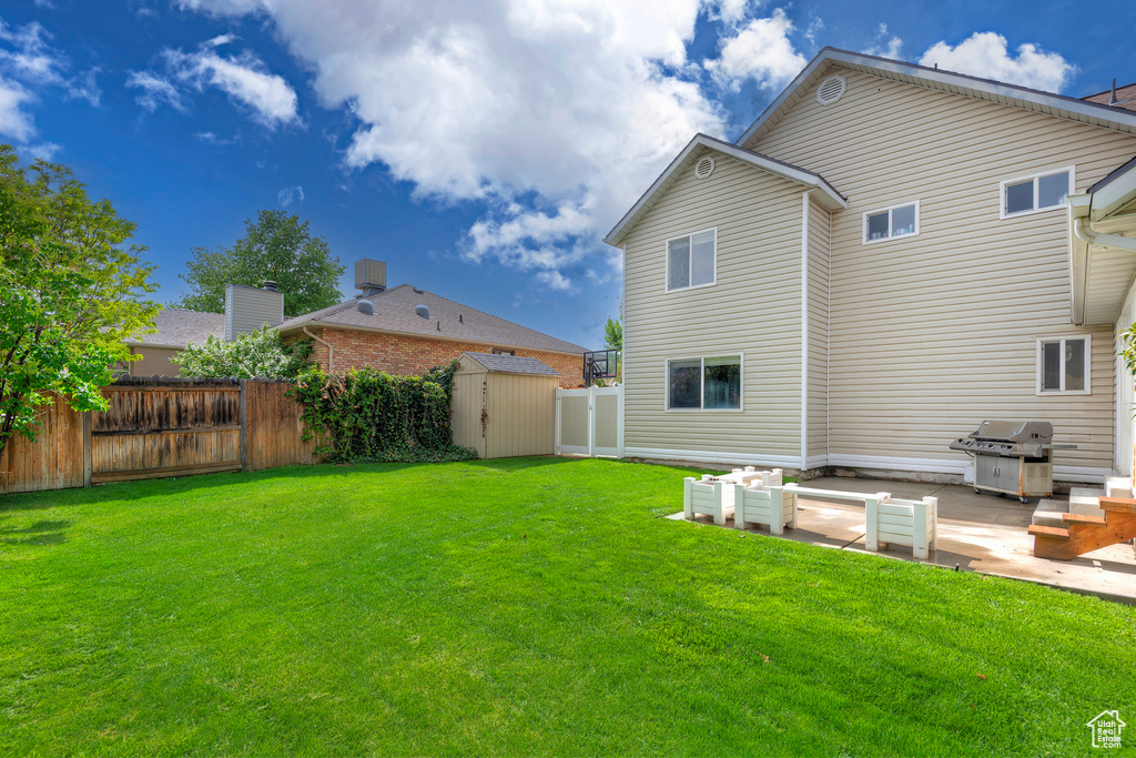 Back of house with a lawn, an outdoor structure, a storage shed, a patio area, and a fenced backyard