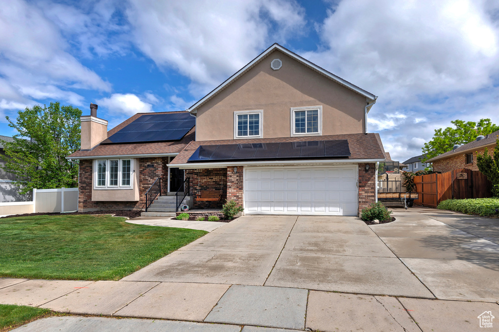 View of front of house featuring brick siding, driveway, solar panels, and a front yard