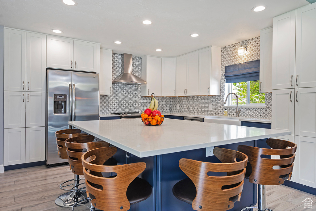 Kitchen with a center island, a sink, white cabinets, wall chimney range hood, and appliances with stainless steel finishes
