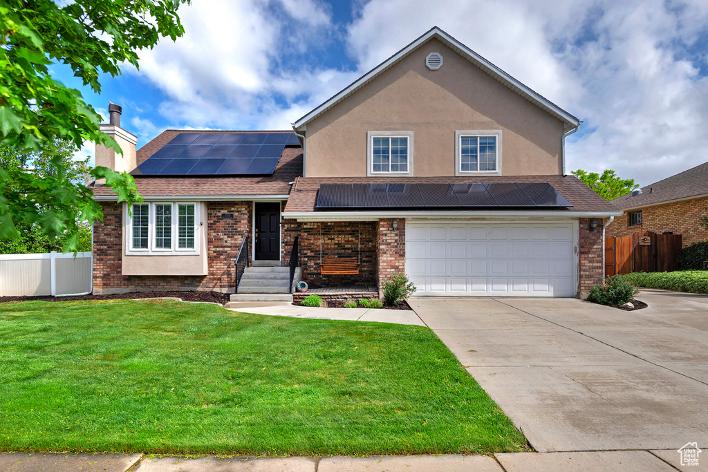 Split level home featuring roof mounted solar panels, a garage, fence, concrete driveway, and a front yard