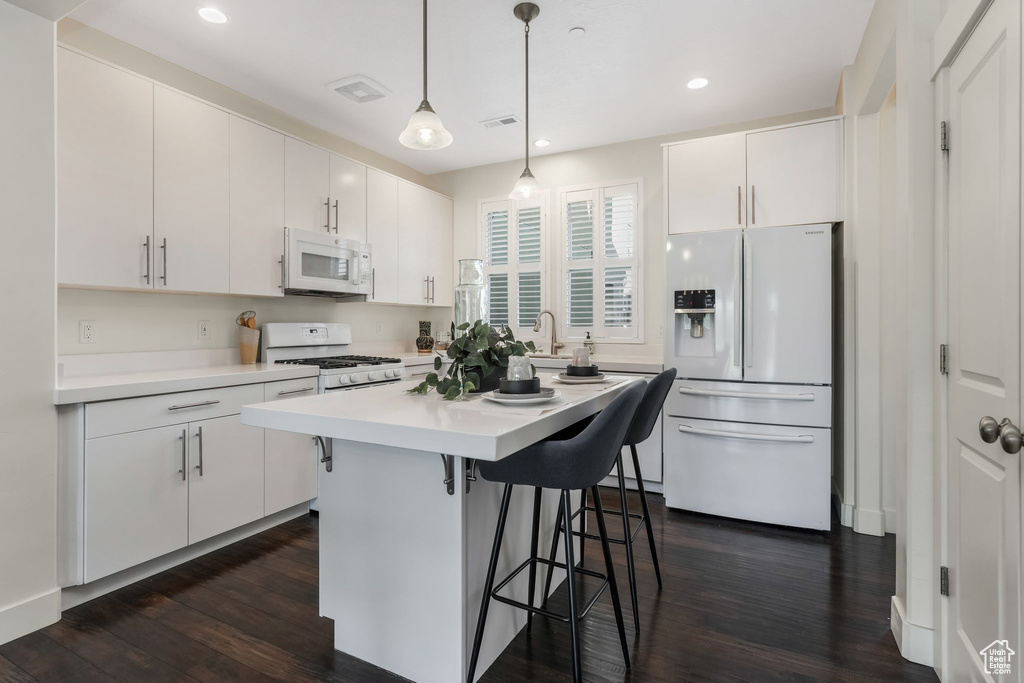 Kitchen featuring white appliances, a kitchen bar, dark wood-type flooring, light countertops, and white cabinetry