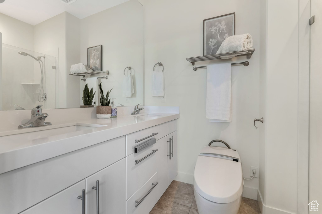 Full bath featuring a shower, toilet, double vanity, tile patterned flooring, and baseboards
