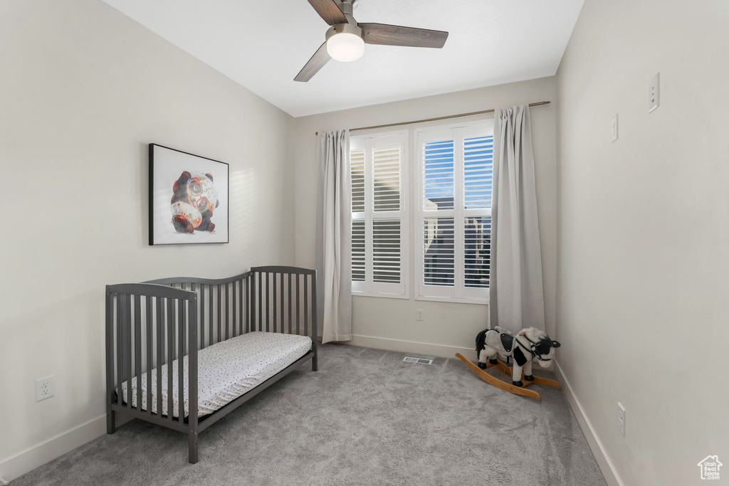 Carpeted bedroom with baseboards, a crib, and ceiling fan