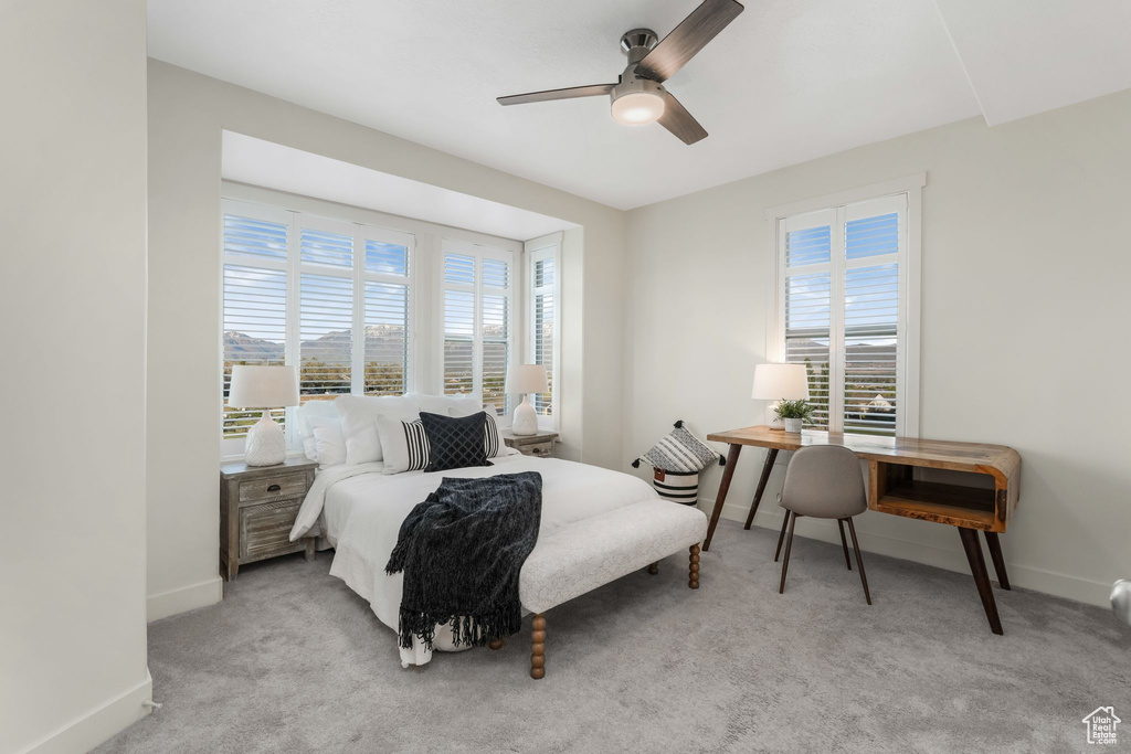 Carpeted bedroom featuring multiple windows, baseboards, ceiling fan, and a desk