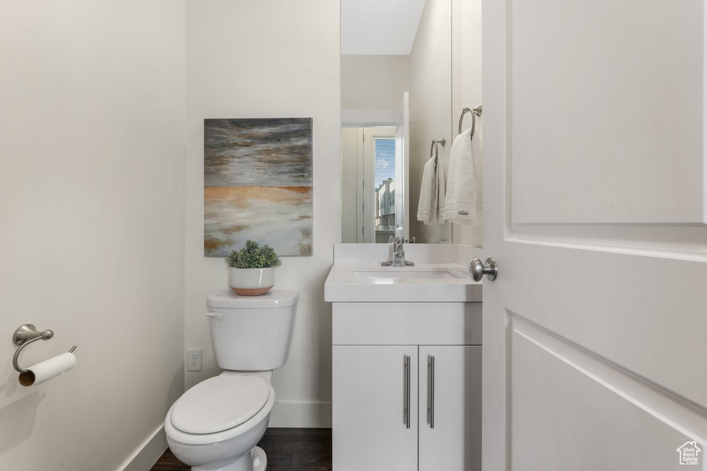 Half bath featuring toilet, vanity, baseboards, and wood finished floors