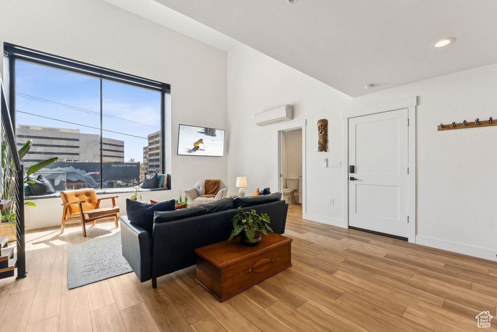 Living room featuring light wood-style floors, a wall mounted AC, recessed lighting, baseboards, and vaulted ceiling