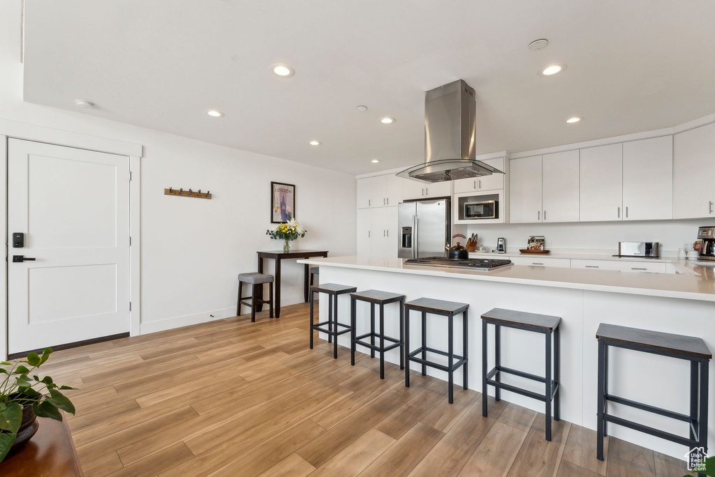 Kitchen with stainless steel appliances, island range hood, a breakfast bar area, light countertops, and light wood finished floors