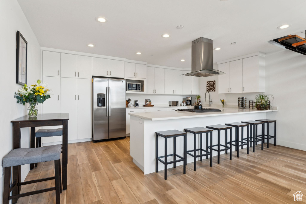 Kitchen with stainless steel appliances, island exhaust hood, a peninsula, a kitchen breakfast bar, and light wood-style floors