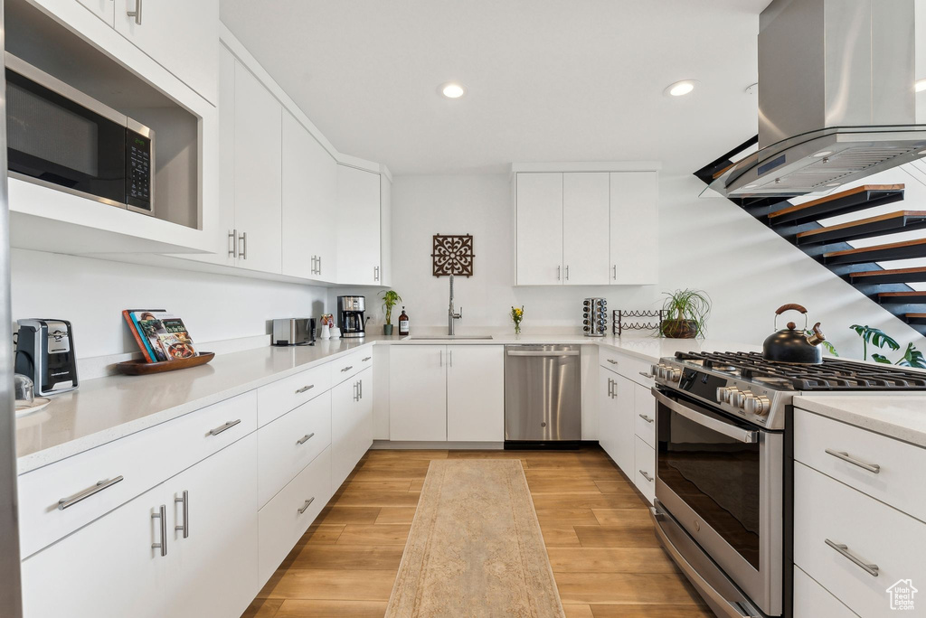 Kitchen with appliances with stainless steel finishes, island range hood, a sink, recessed lighting, and light countertops