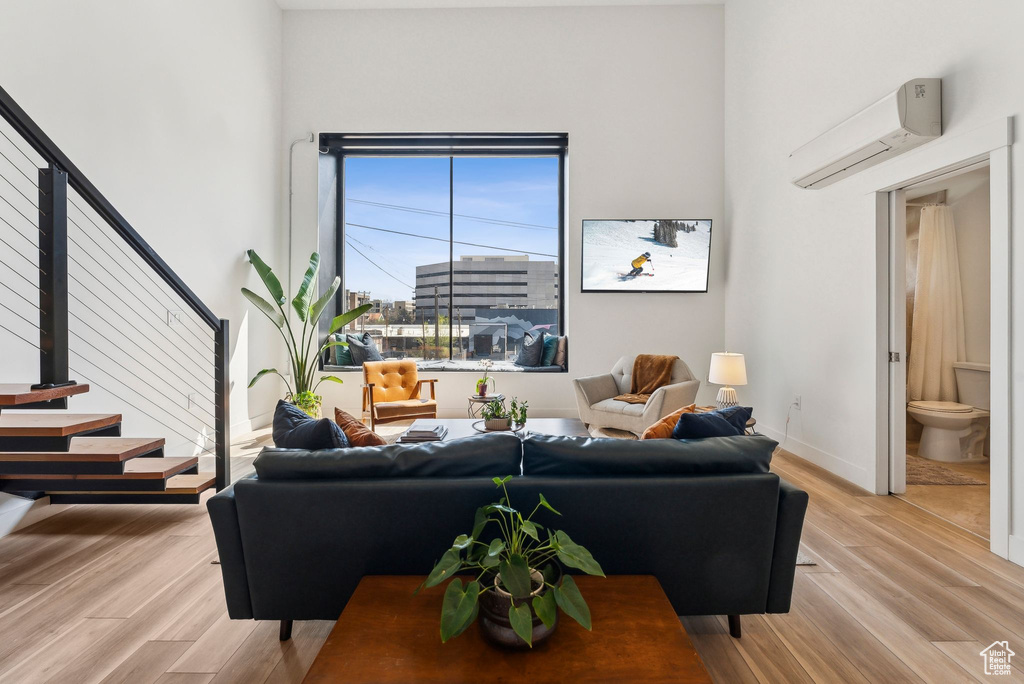 Living room with a wall unit AC, light wood-style floors, stairs, and baseboards