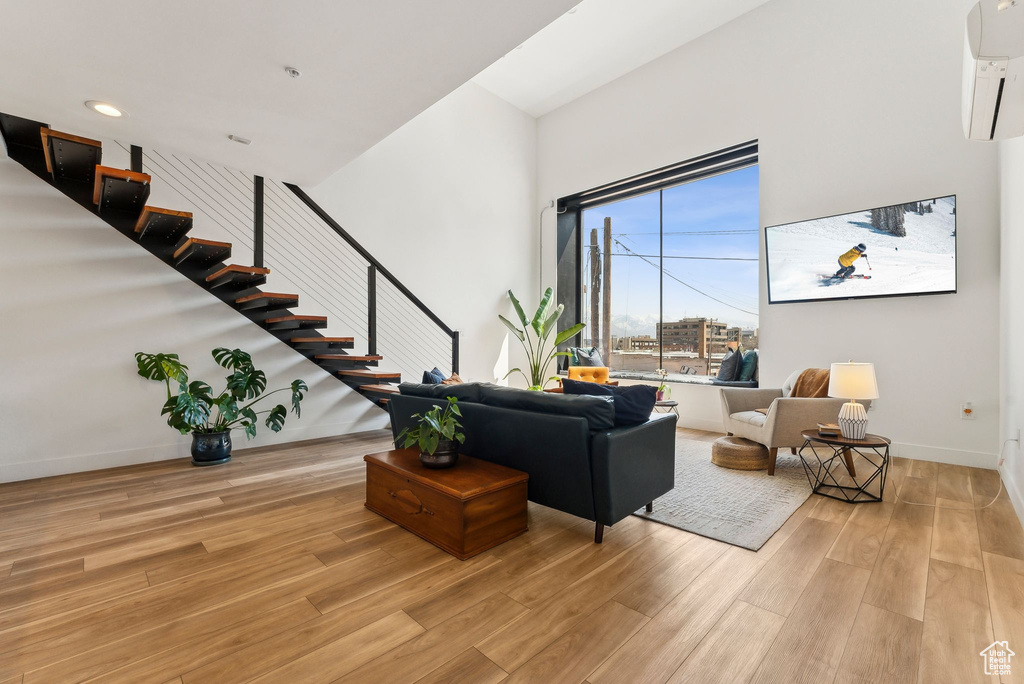 Living room with stairway, an AC wall unit, light wood-style floors, baseboards, and a high ceiling