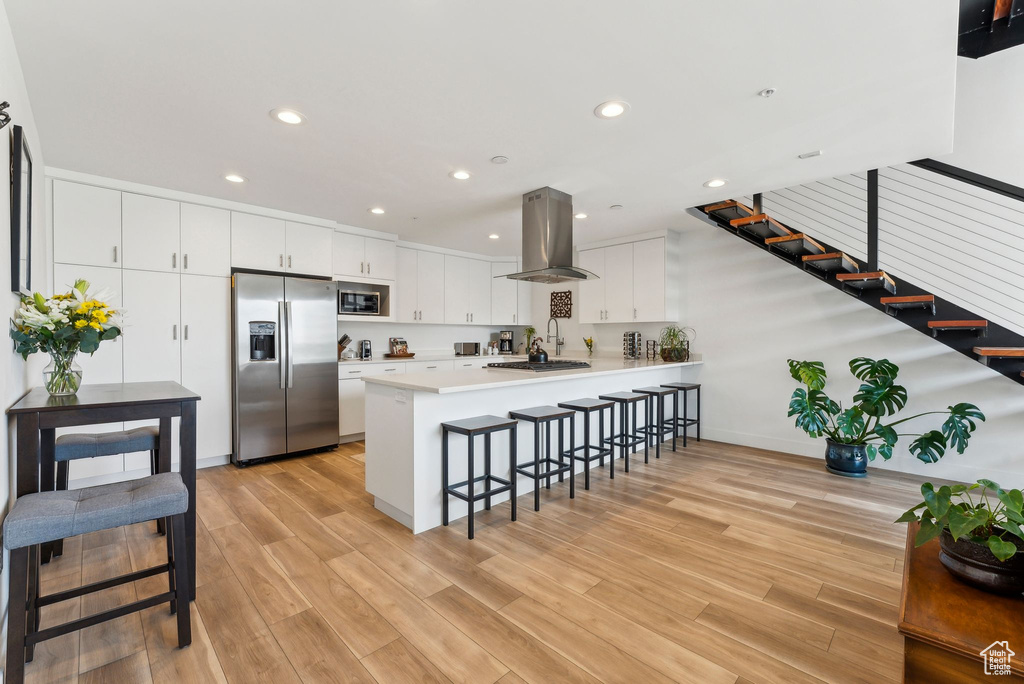 Kitchen featuring stainless steel appliances, island exhaust hood, a peninsula, a kitchen breakfast bar, and recessed lighting