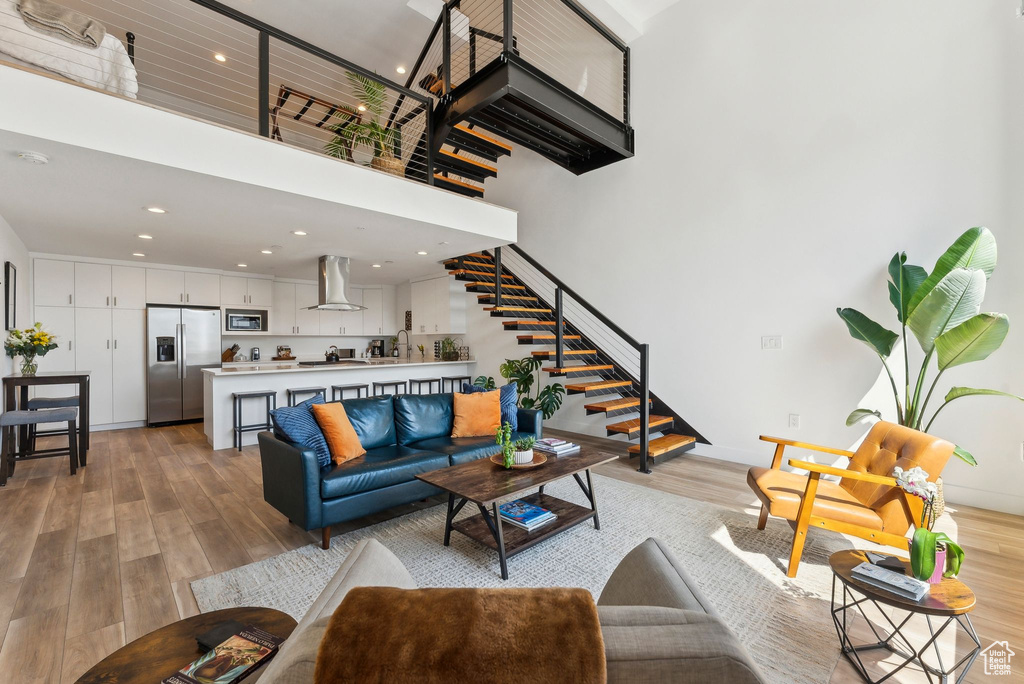 Living room with a high ceiling, light wood finished floors, stairs, recessed lighting, and baseboards